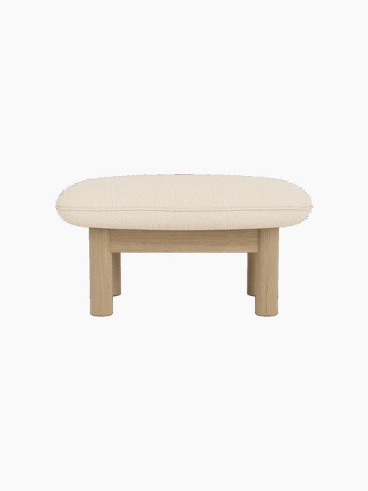 A side view of the Brasilia Ottoman with a natural oak frame and a light beige Logan Jasmine cushion on a black background.