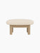A side view of the Brasilia Ottoman with a natural oak frame and a light beige Logan Jasmine cushion on a black background.