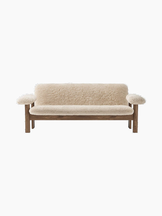 Front view of the Brasilia Sofa with a natural wood frame and off-white sheepskin upholstery against a black background.