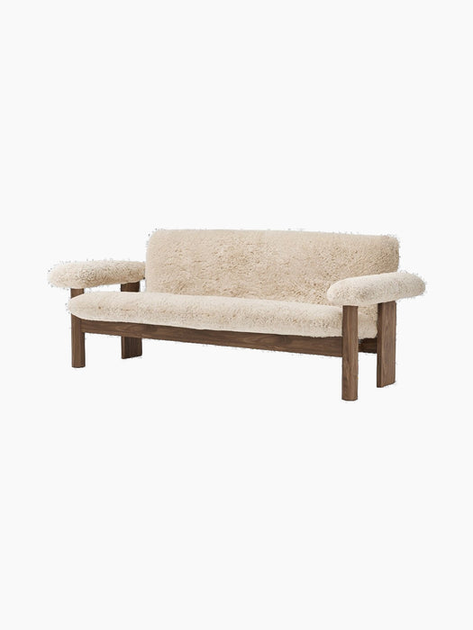 The Brasilia Sofa in Sheepskin at an angle, with a dark wood frame and plush, light sheepskin upholstery.