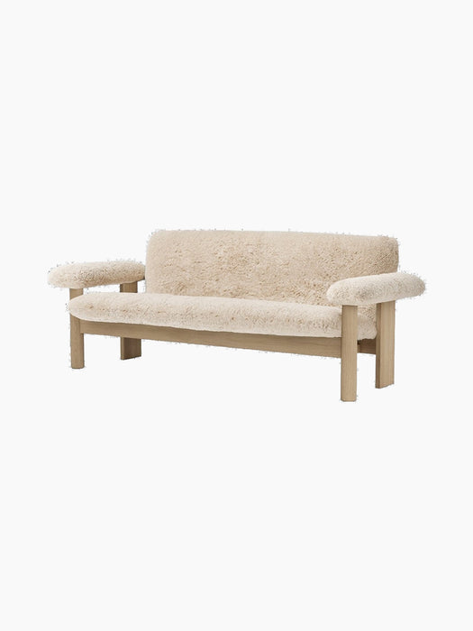 Angled view of the Brasilia Sofa, upholstered in plush cream Sheepskin with a light oak frame and large rounded armrests.