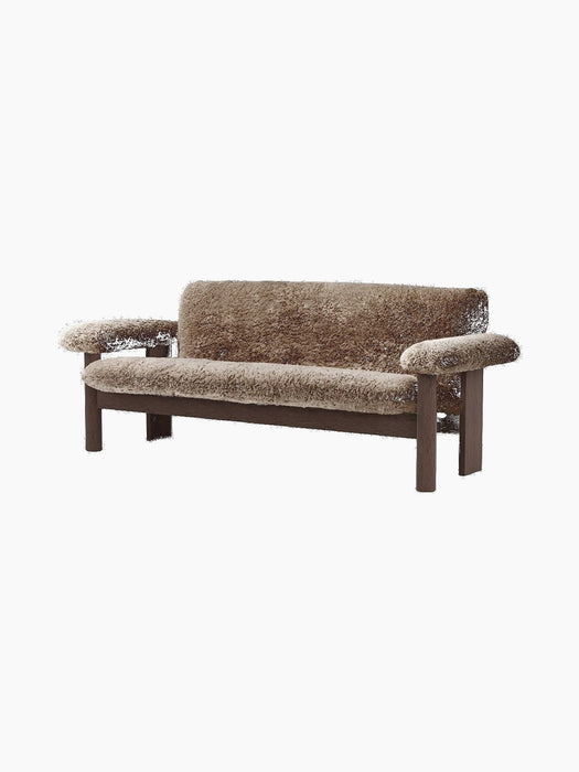 The Brasilia Sofa, upholstered in thick brown sheepskin, with a dark wood frame featuring chunky, rounded legs and armrests.