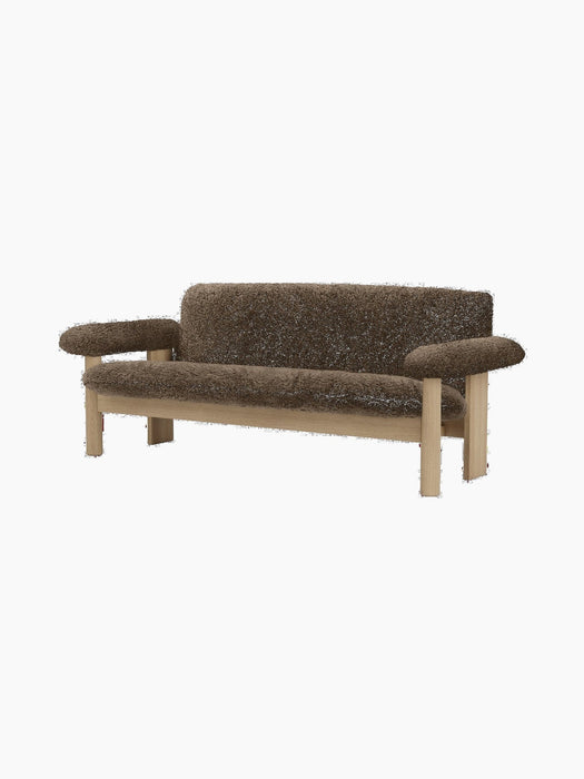 Angled view of the Brasilia Sofa with a natural oak frame and upholstered in dark brown Sheepskin, on a black background.