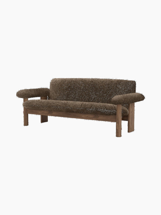 The Brasilia Sofa in dark brown sheepskin, with a dark wood frame and exaggerated, rounded armrests, shown from an angle.