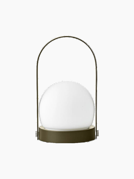 A back view of the Carrie Portable Table Lamp in olive, with its round olive base, white glass orb and thin handle.