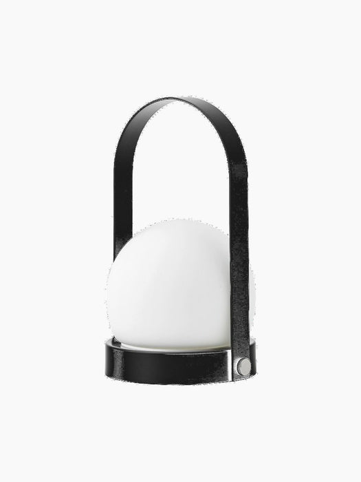 The black Carrie Table Lamp, Portable shown from an angle. It has a white glass orb, a circular base and a matching handle.