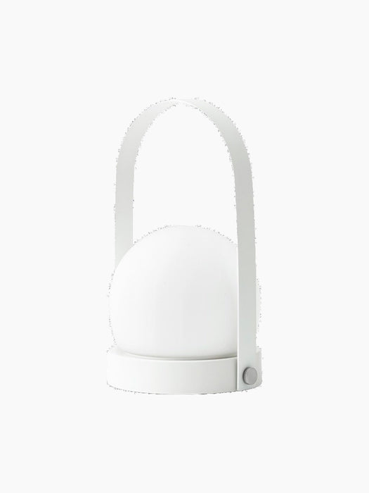 A white portable Carrie Table Lamp shown at an angle. It features a round base, arched handle, and spherical glass shade.