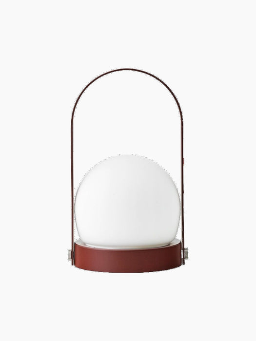 Back view of the portable Carrie Table Lamp in Burned Red, featuring a slim handle arching over a glowing white glass orb.