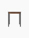 A front-on view of the rectangular Co Table, featuring a dark wood-grain laminate top and slender black steel legs.