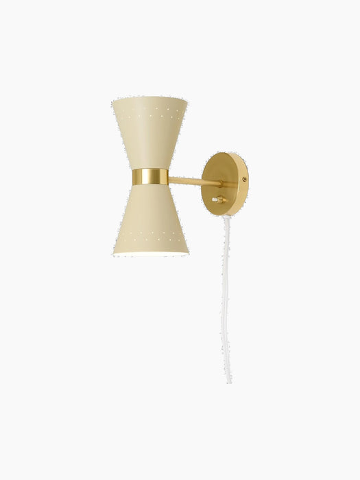 The Collector Wall Lamp in cream with a polished brass fixture. The illuminated hourglass shade has perforated details.