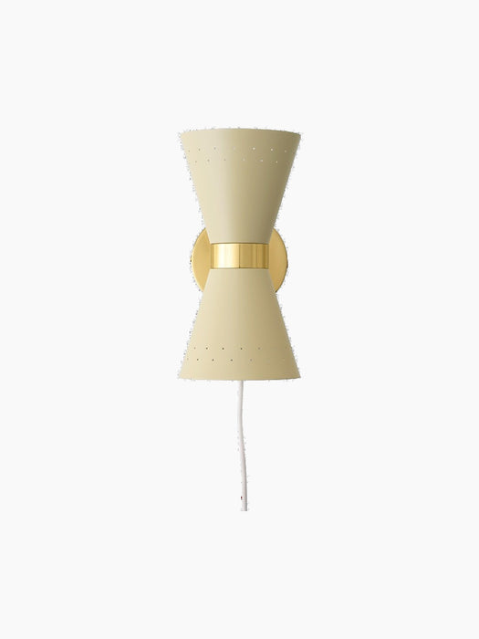 The cream Collector Wall Lamp, front view. Hourglass-shaped with perforated shades, a brass band, and a white power cord.