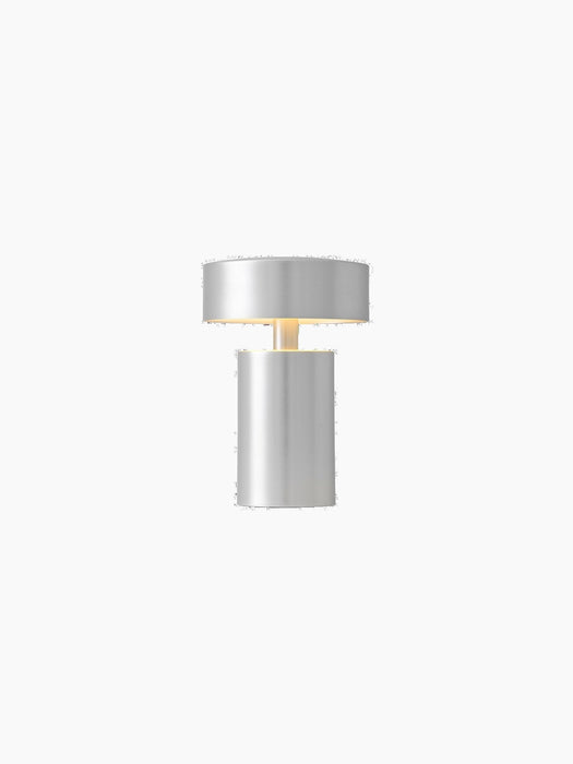 Portable Column Table Lamp in brushed aluminium, illuminated with a warm glow and isolated against a black background.