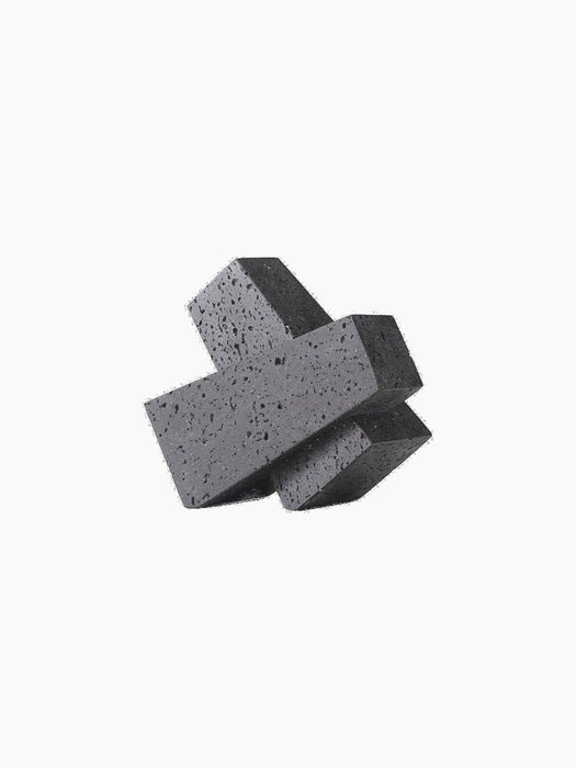 A dark grey, porous stone Converge Book End with an interlocking, geometric shape, shown at an angle on a black background.