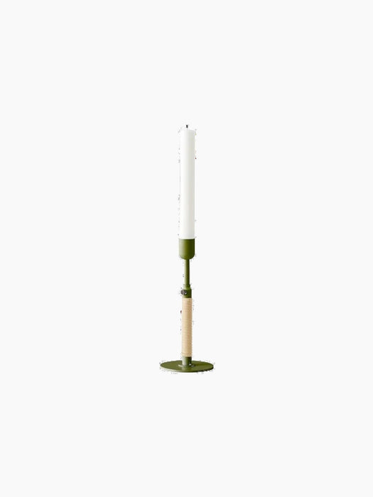 The tall, slender Duca Candle Holder in olive green with a rattan handle, holding a white candle on a black background.