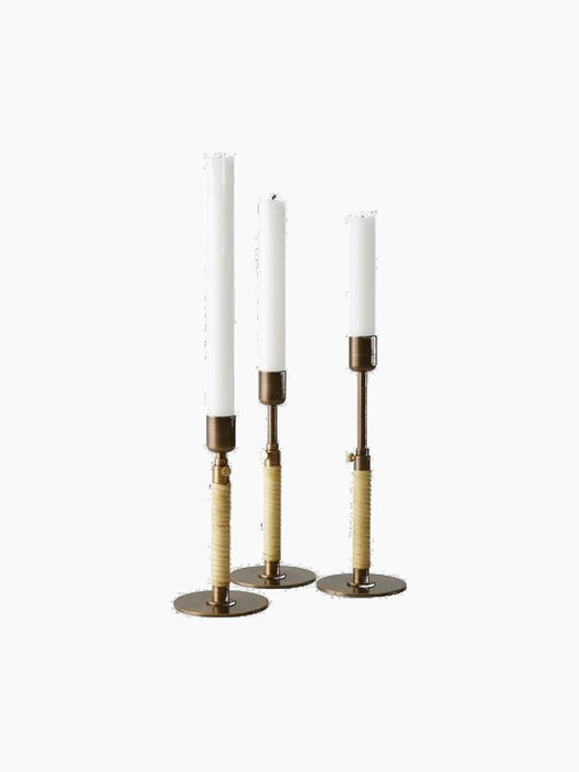 Three Duca Candlesticks in Bronzed Brass with rattan-wrapped stems holding white candles, shown against a black background.