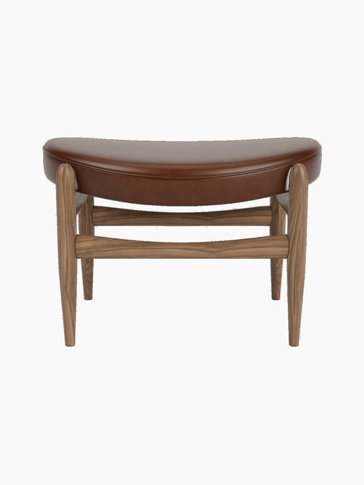 Front view of the Elizabeth Ottoman with a curved brown leather seat and a solid walnut frame on a black background.