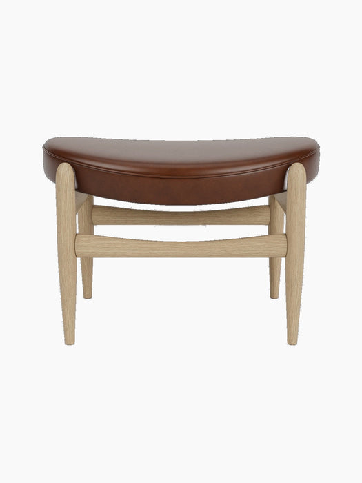 A front view of the Elizabeth Ottoman, featuring a curved brown leather seat and a light natural oak frame.