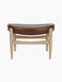 A front view of the Elizabeth Ottoman, featuring a curved brown leather seat and a light natural oak frame.