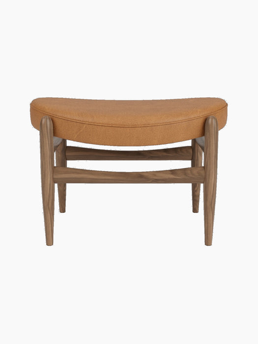 Front view of the Elizabeth Ottoman. The piece has a walnut frame and a curved top cushion upholstered in cognac leather.