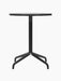 A front view of the Harbour Column Dining Table with a round black oak top and black star base, on a black background.