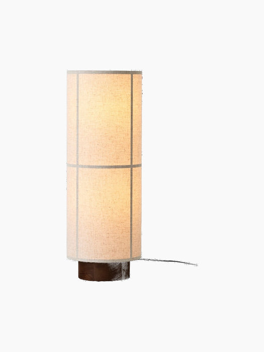 A studio shot of the Hashira Floor Lamp, Raw. The cylindrical linen shade is illuminated, revealing a grid on a wood base.