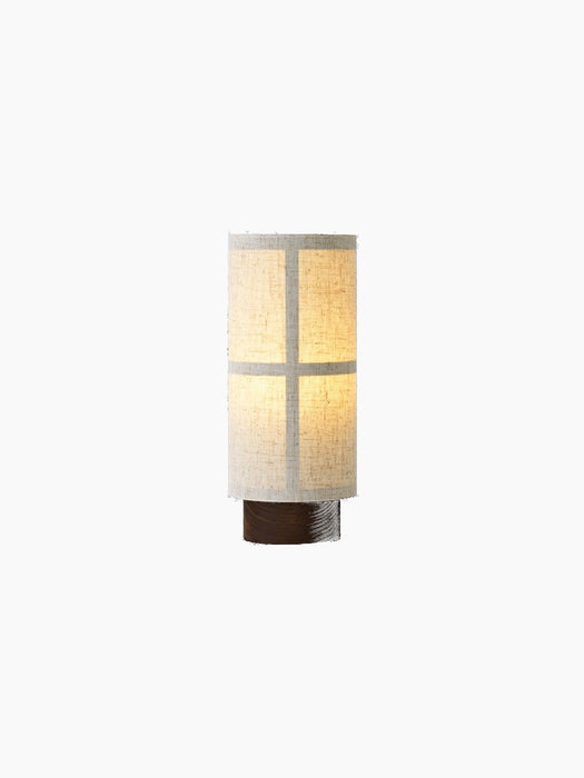 Hashira Portable Table Lamp, front view. Its illuminated raw linen shade reveals a grid frame and sits on a dark ash base.