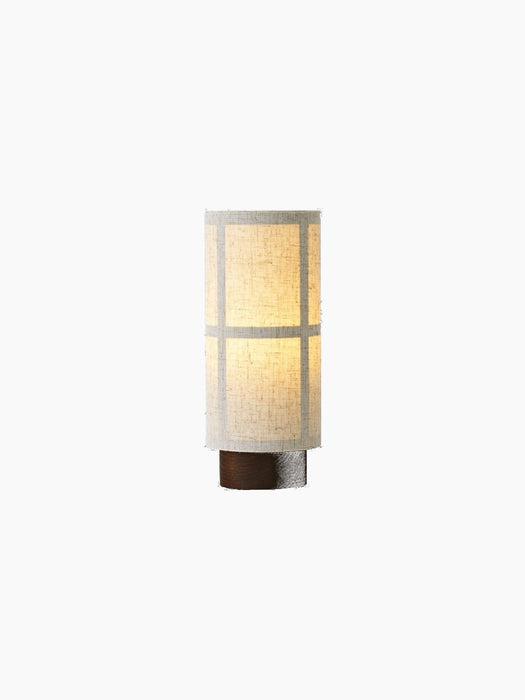 Illuminated Hashira Portable Table Lamp with a cylindrical raw linen shade featuring a grid pattern, on a dark wood base.