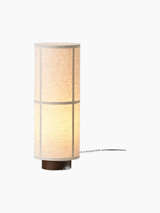 Front view of the Hashira Table Lamp in Raw, illuminated. It features a cylindrical linen shade on a dark ash wood base.