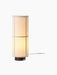 Front view of the Hashira Table Lamp in Raw, illuminated. It features a cylindrical linen shade on a dark ash wood base.