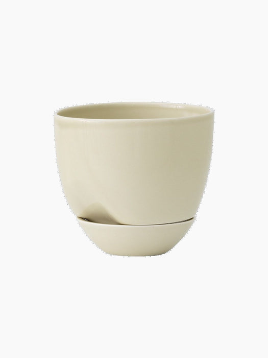 The Hydrous Planter in a pale, off-white Ashen finish. A rounded ceramic planter with a notch and matching saucer.