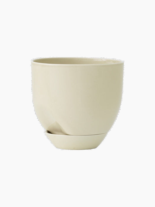 Angled view of the Hydrous Planter O20 in Ashen, a rounded, cream ceramic pot with a drainage spout and matching saucer.