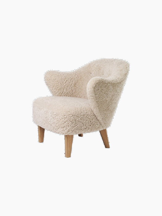 A three-quarter view of the Ingeborg Lounge Chair in fluffy, off-white Sheepskin Moonlight with four angled natural oak legs.