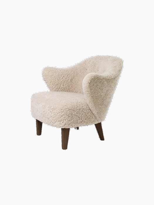 Angled view of the Ingeborg Lounge Chair, upholstered in fluffy off-white Moonlight sheepskin, with dark-stained oak legs.