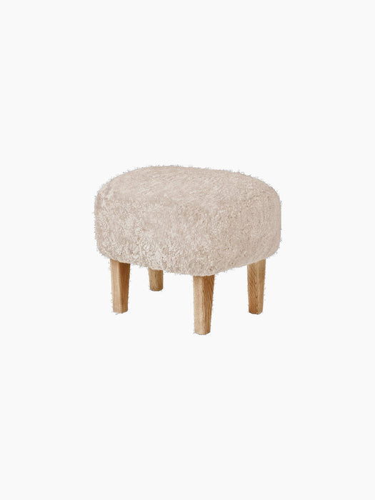 A three-quarter view of the Ingeborg Ottoman. The oval stool has a fluffy, off-white Sheepskin Moonlight seat and oak legs.