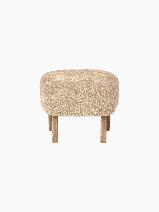 A front-facing view of the Ingeborg Ottoman. It has a fluffy, honey-coloured sheepskin top and four light oak legs.