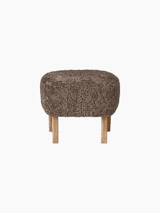 The oval Ingeborg Ottoman with a cushioned top upholstered in curly Sahara sheepskin on four short natural oak legs.