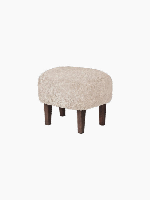 A frontal view of the Ingeborg Ottoman, upholstered in fluffy Moonlight Sheepskin with four dark-stained wooden legs.