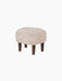 A frontal view of the Ingeborg Ottoman, upholstered in fluffy Moonlight Sheepskin with four dark-stained wooden legs.