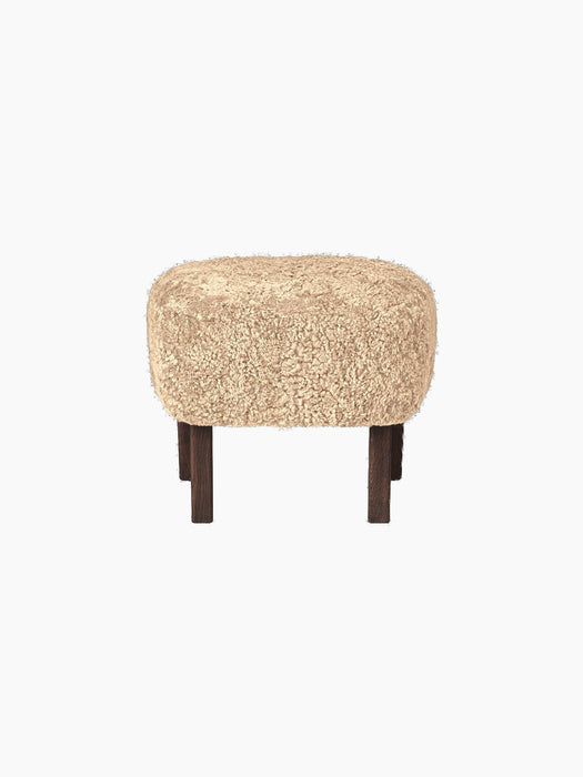 Side view of the Ingeborg Ottoman with a plush, honey-coloured sheepskin seat and short, dark-stained oak legs.