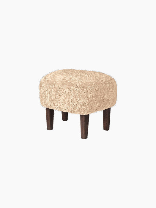 Ingeborg Ottoman with a round, honey-coloured sheepskin top and four short, dark-stained oak legs, on a black background.