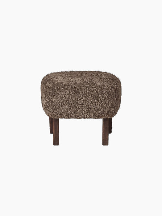 A studio shot of the Ingeborg Ottoman in Sahara sheepskin. The footstool has a textured, brownish top and four dark oak legs.