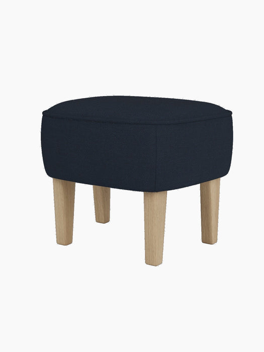 The Ingeborg Ottoman, with a dark blue textured textile seat and natural oak legs, viewed from a front-three-quarter angle.