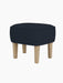 The Ingeborg Ottoman, with a dark blue textured textile seat and natural oak legs, viewed from a front-three-quarter angle.