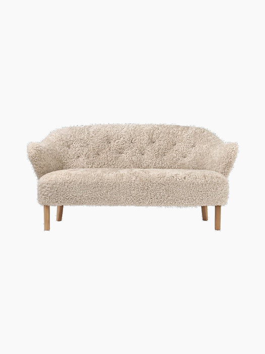 Front view of the Ingeborg Sofa in off-white Moonlight sheepskin, featuring a button-tufted back, flared arms, and oak legs.