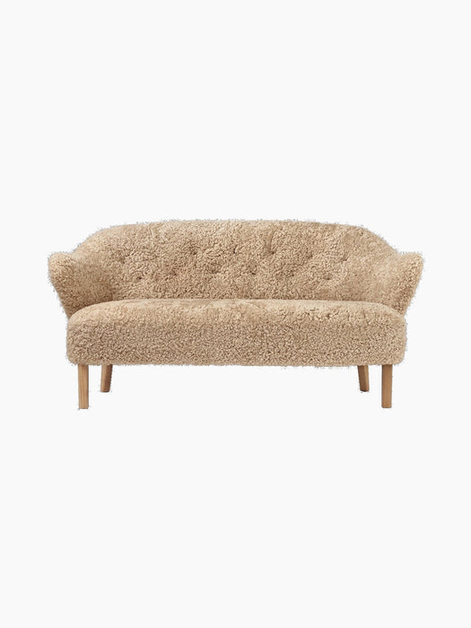 A front view of the Ingeborg Sofa, upholstered in textured honey sheepskin. It has a buttoned back and natural oak legs.