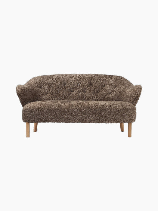 Front view of the Ingeborg Sofa in textured, brown Sahara sheepskin, featuring a button-tufted back and light oak legs.