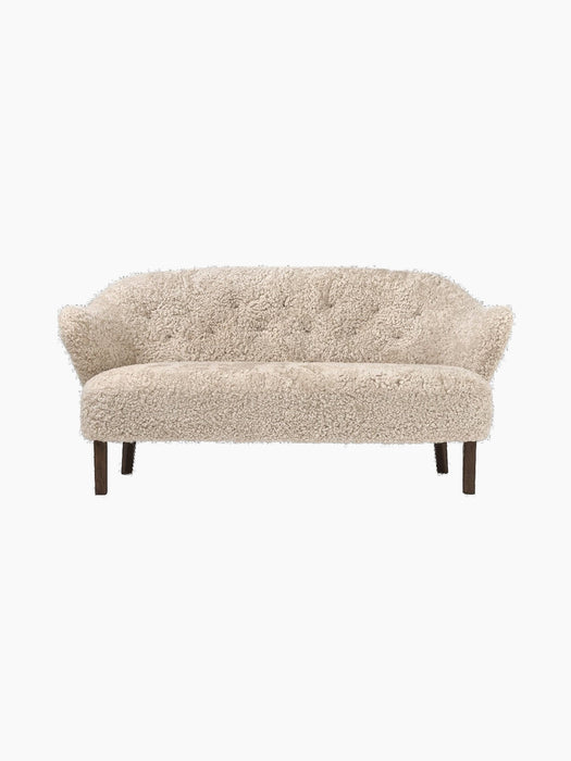 Front view of the Ingeborg Sofa in Moonlight sheepskin upholstery. The elegant sofa has a buttoned back and dark wood legs.