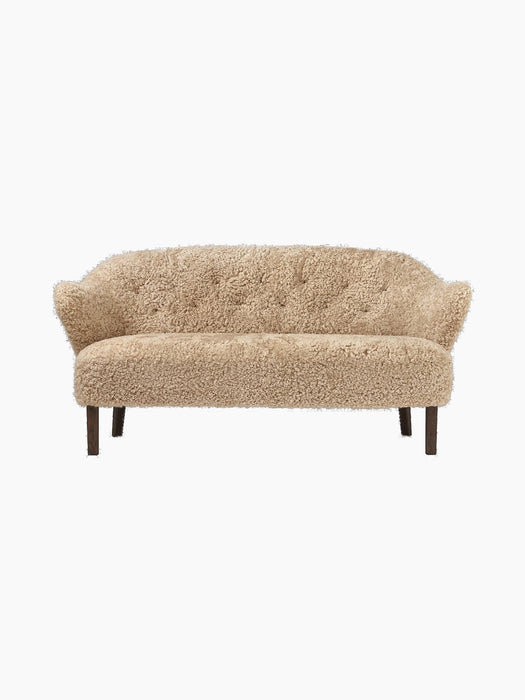 Front view of the Ingeborg Sofa in honey-coloured sheepskin, featuring a button-tufted back, curved arms, and dark oak legs.