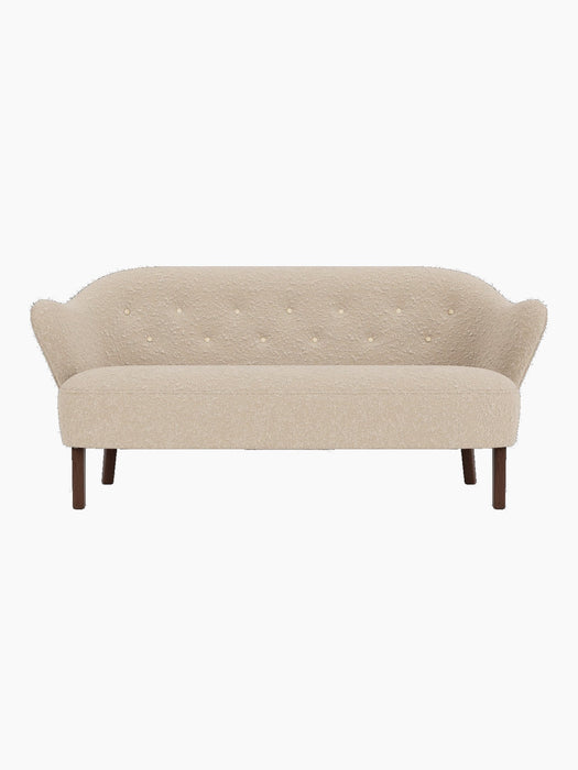 Front view of the Ingeborg Sofa in a textured light beige fabric with a buttoned back, flared arms and smoked oak legs.