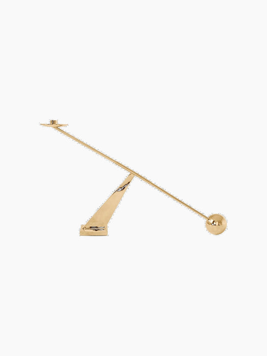 A side view of the sculptural Interconnect Candle Holder in polished brass, balanced on a triangular base.
